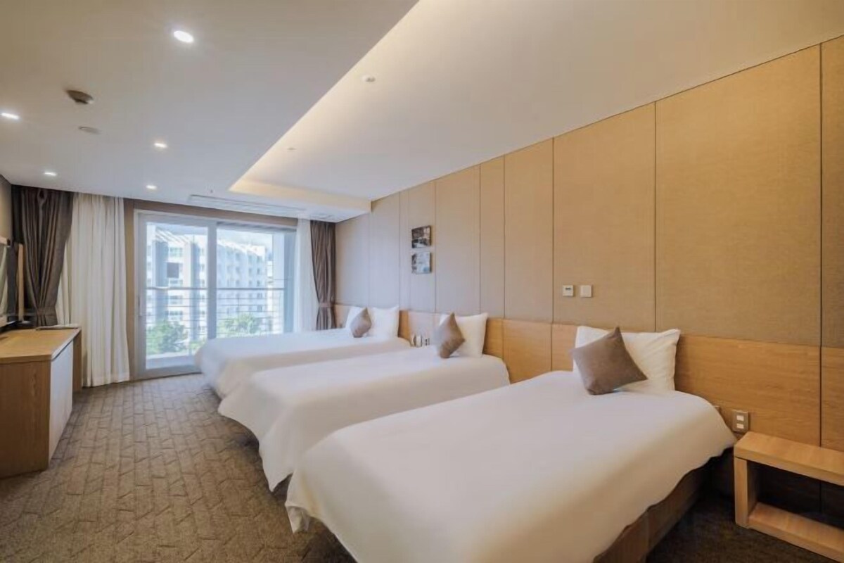 A hotel room with two beds, a desk, and a large window.
