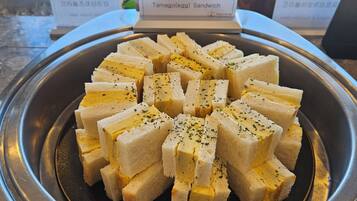 A tray of tamago (egg) sandwiches garnished with herbs, displayed on a metal stand with a sign above.