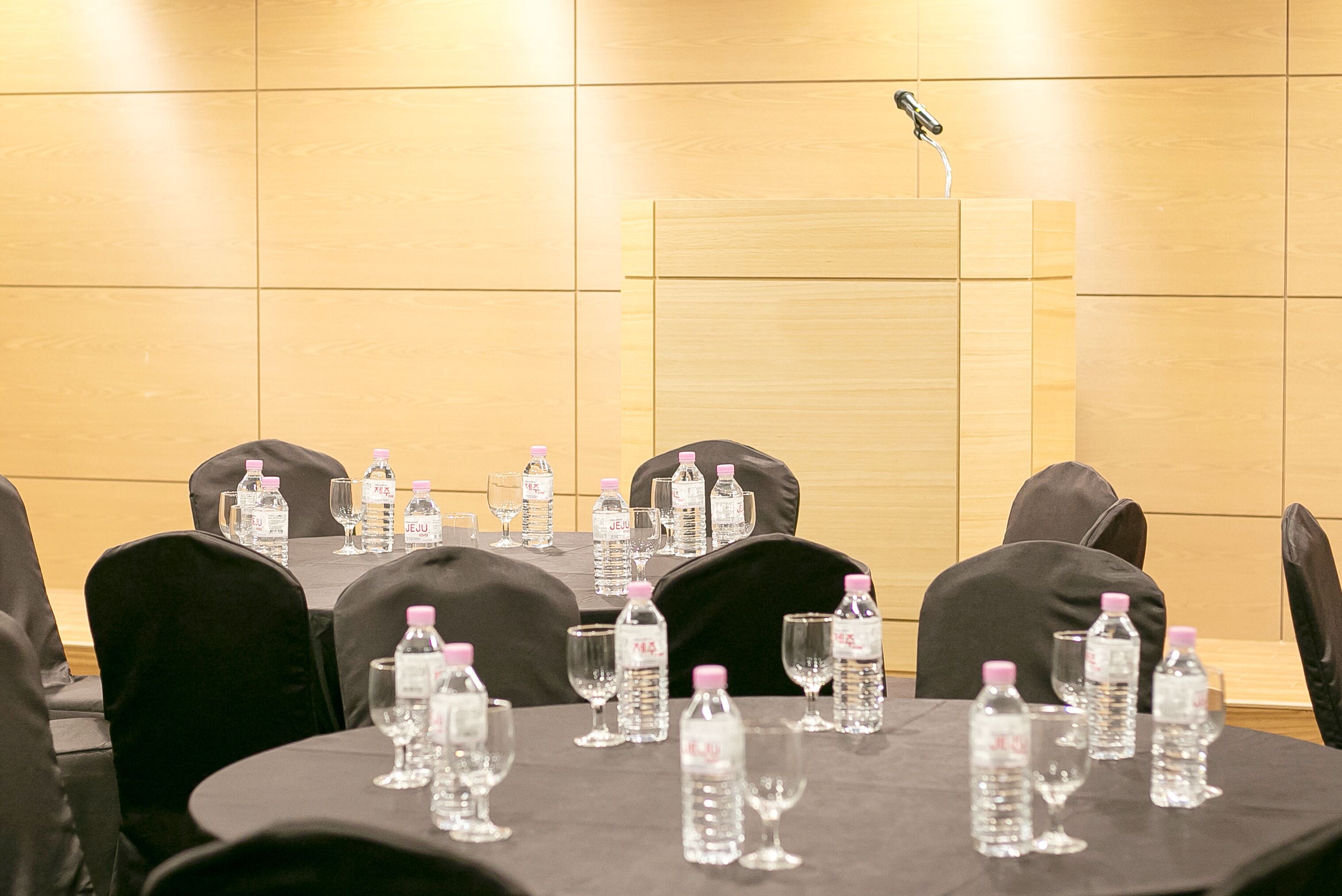 Un salón de conferencias con mesas dispuestas para una reunión, equipado con botellas de agua y vasos.
