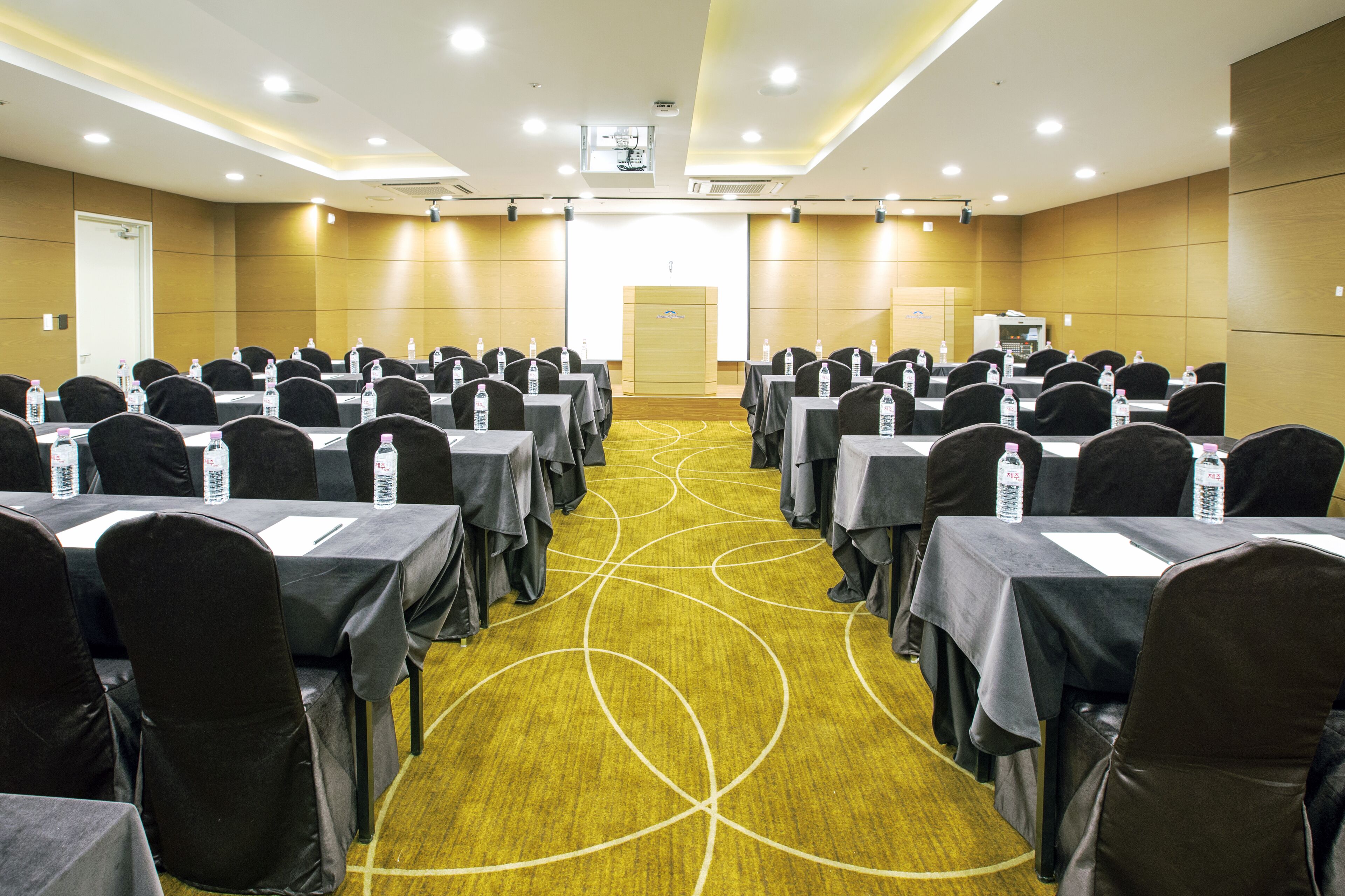 Una sala conferenze con file di tavoli e sedie, dotata di bottiglie d'acqua e cartellini con i nomi.