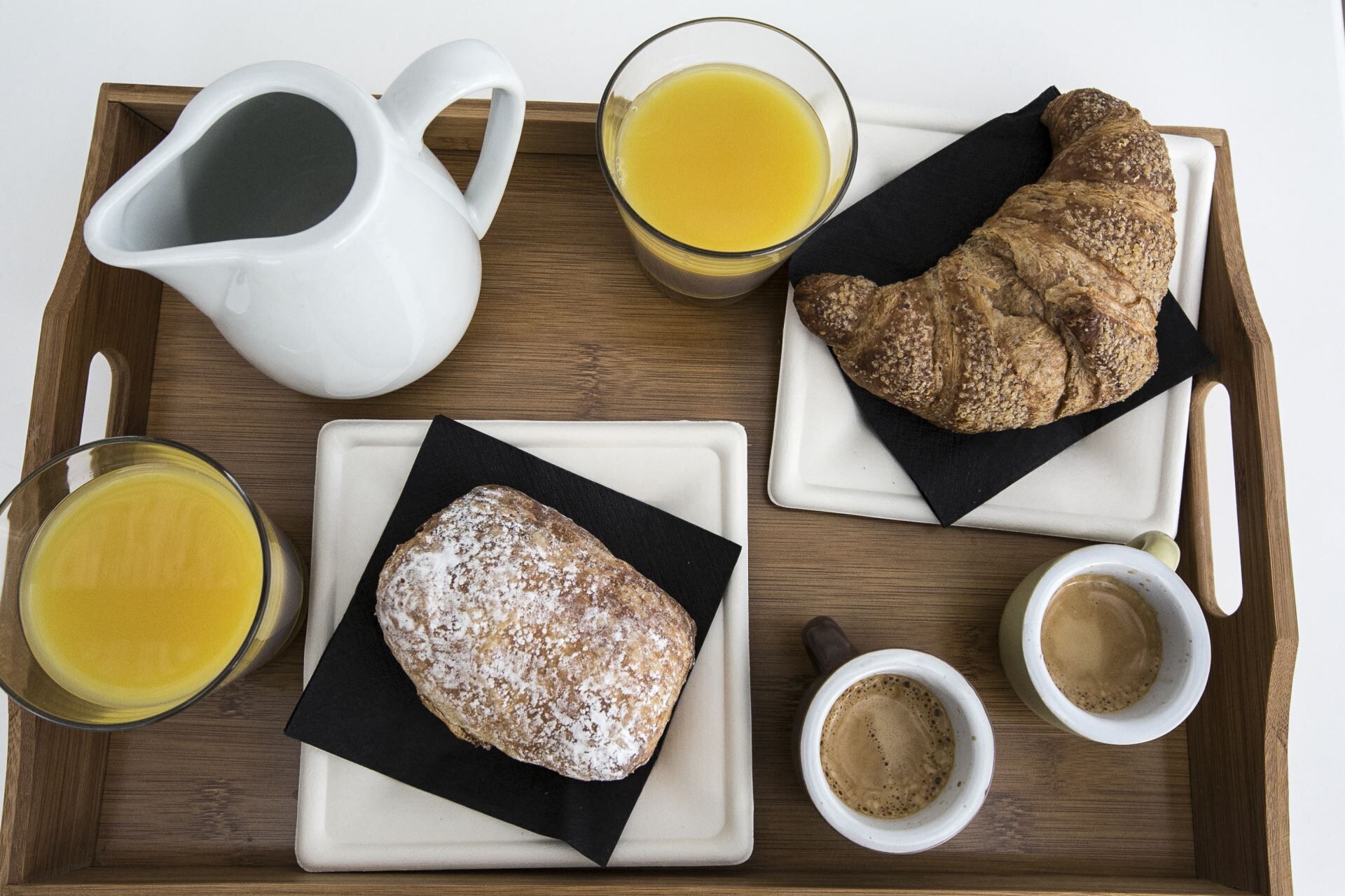 A tray with a croissant, two glasses of orange juice, a white pitcher, and two small cups of coffee.