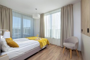A modern hotel room with a bed, a chair, a bedside table with a lamp, and a window with curtains.