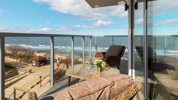 A balcony with a glass table, wicker chairs, and a view of the ocean.