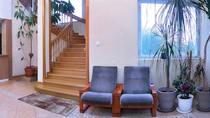 A reception area with a wooden desk, two grey armchairs, a staircase, and potted plants. - Penzión DRUŽBA Bojnice (Bojnice)