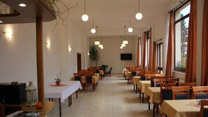 A spacious dining area with multiple tables and chairs, a television mounted on the wall, and large windows with curtains. - Penzión DRUŽBA Bojnice (Bojnice)