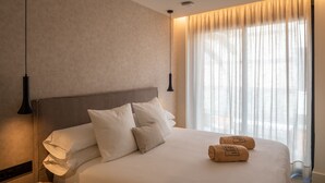 Une chambre d’hôtel avec un grand lit, une table de chevet, une lampe et une fenêtre avec des rideaux légers.
