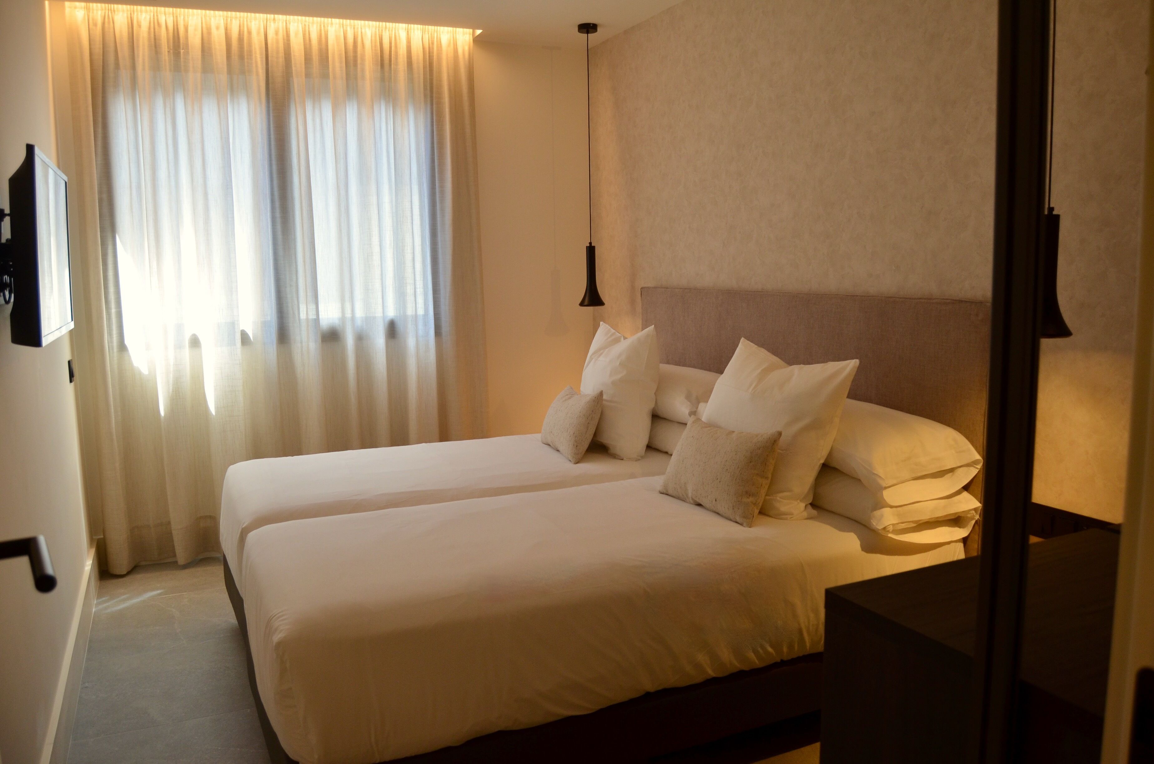 A hotel room with two beds, a flat-screen TV, and a large window with curtains.