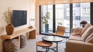 Un salon moderne avec un canapé, une table basse, un téléviseur et un balcon agrémenté d’une chaise et d’une plante.
