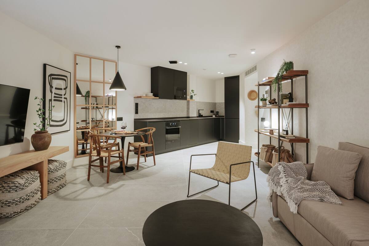 Un salon moderne comprenant un canapé, une table à manger avec des chaises, un coin cuisine avec des meubles sombres et un téléviseur fixé au mur.