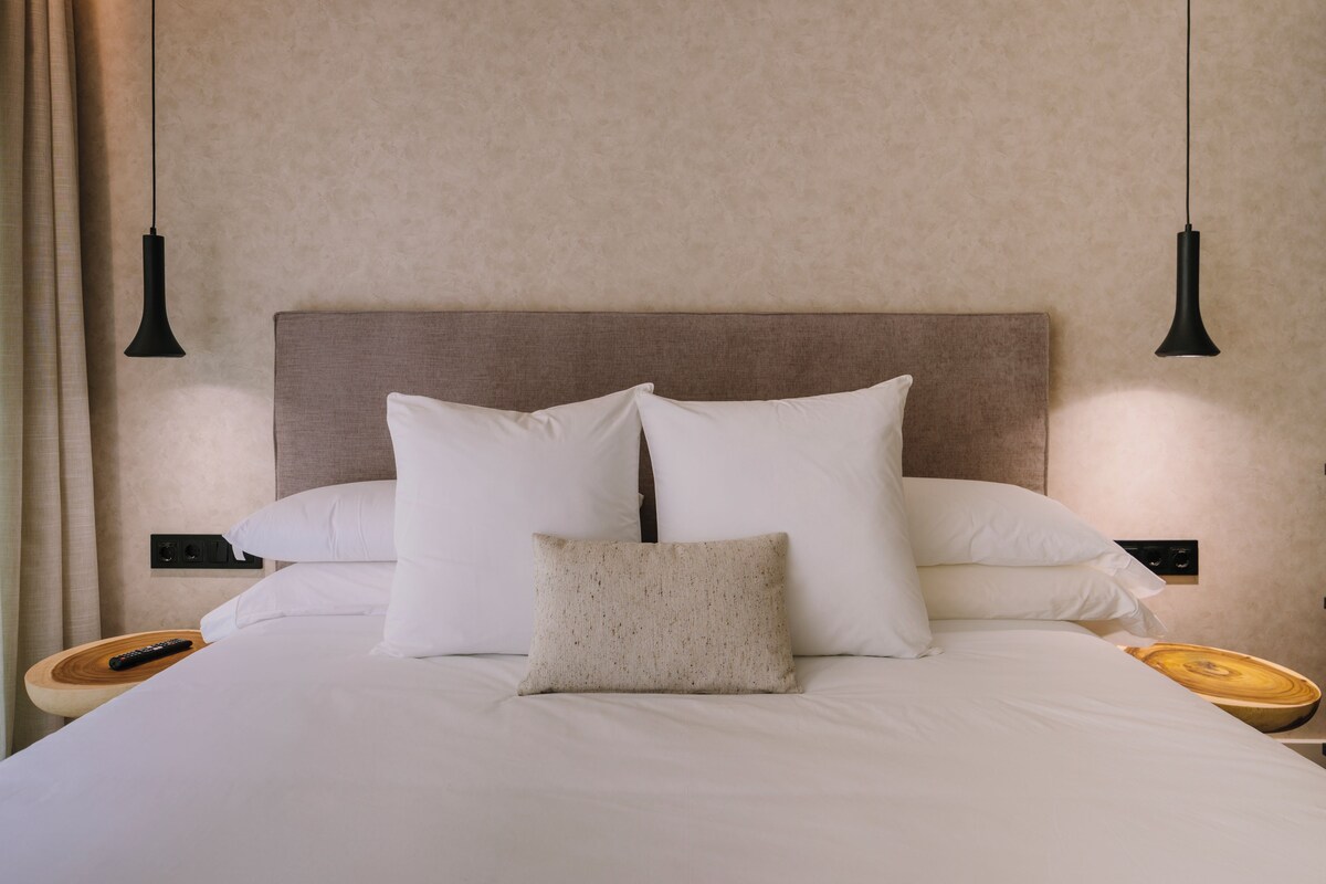A neatly made bed with white linens and pillows, a wooden headboard, and two bedside tables with black lamps.