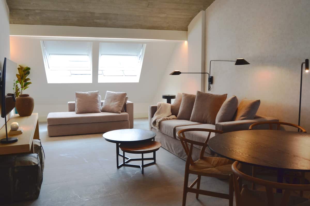 Un salon moderne avec un canapé, deux tables rondes et un plafond avec des poutres apparentes.