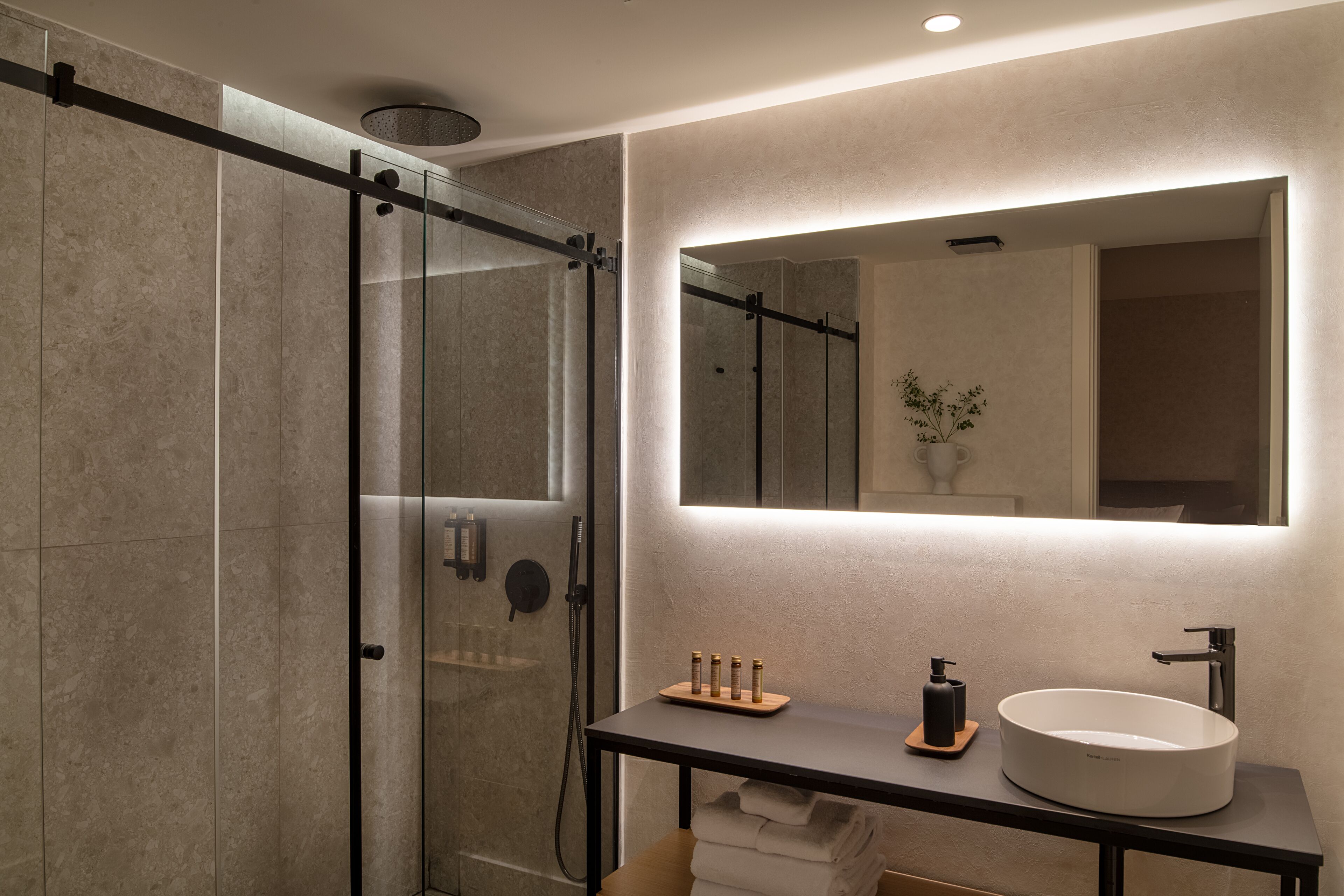 Un baño moderno con cabina de ducha de vidrio, un lavabo redondo e iluminación integrada en el espejo.