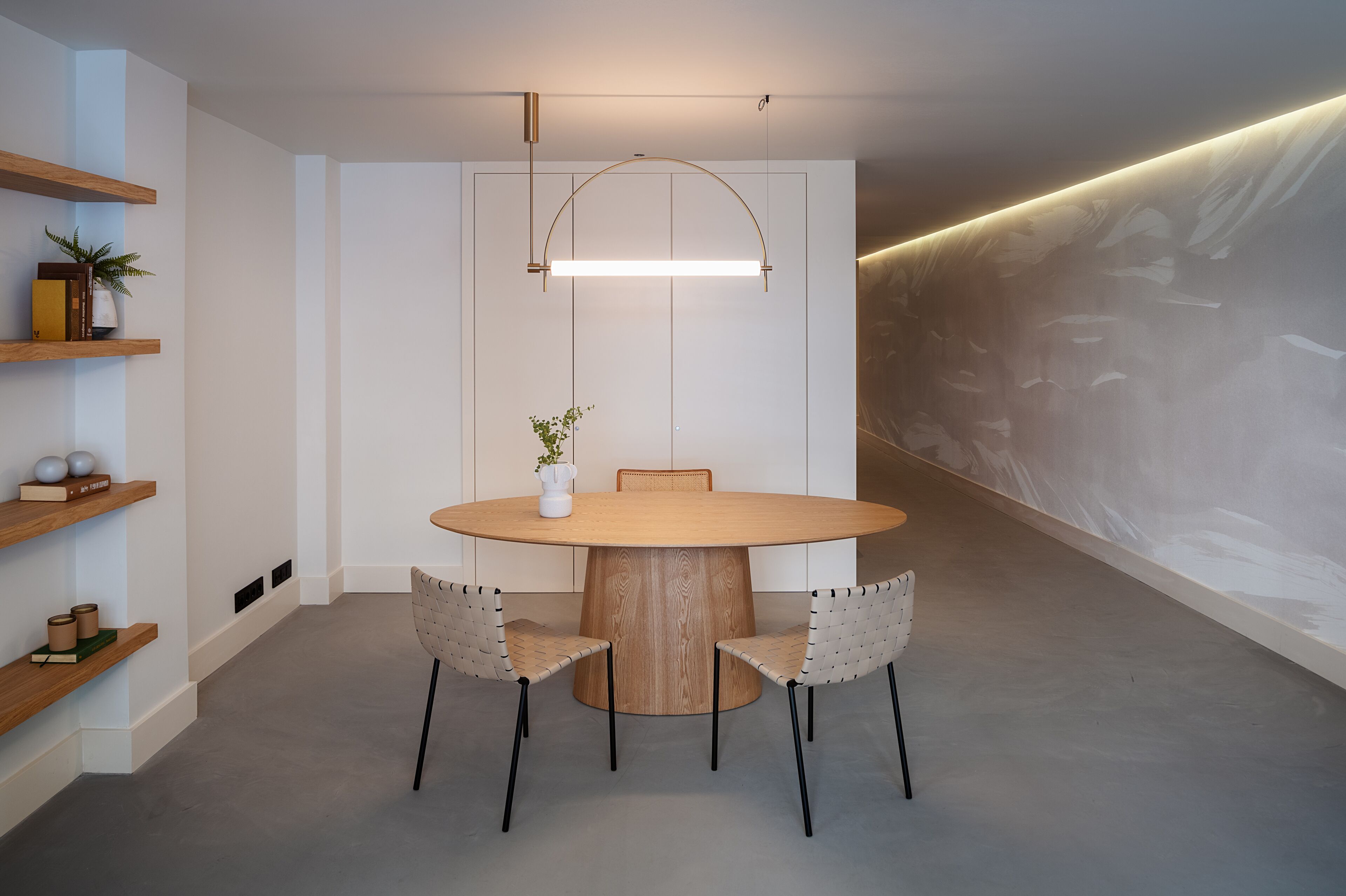 A modern dining area with a round wooden table, two chairs, a vase with a plant, and a pendant light.