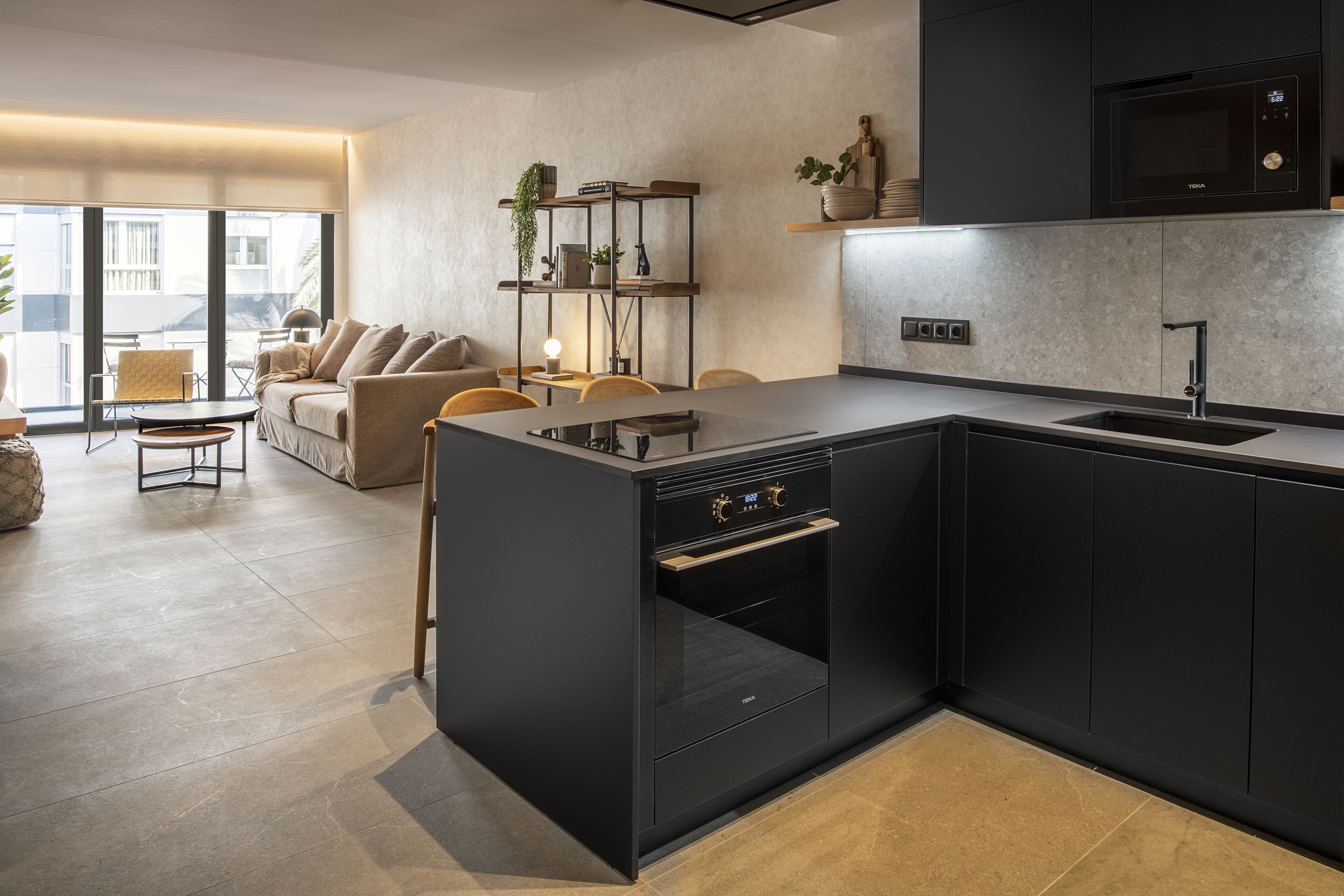 A modern kitchen with black cabinetry, a built-in oven, and a dining area with a sofa and chairs.