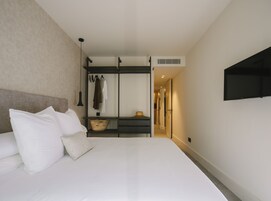 A hotel room with a bed, a wardrobe, a flat-screen TV, and a hallway leading to another room.