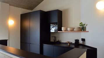A modern kitchen with dark cabinetry, a wooden countertop, and a built-in oven. There are white plates and a vase on a shelf above the counter.