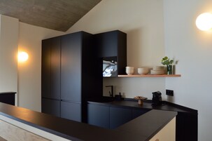 A modern kitchen with dark cabinetry, a wooden countertop, and a built-in oven. There are white plates and a vase on a shelf above the counter.