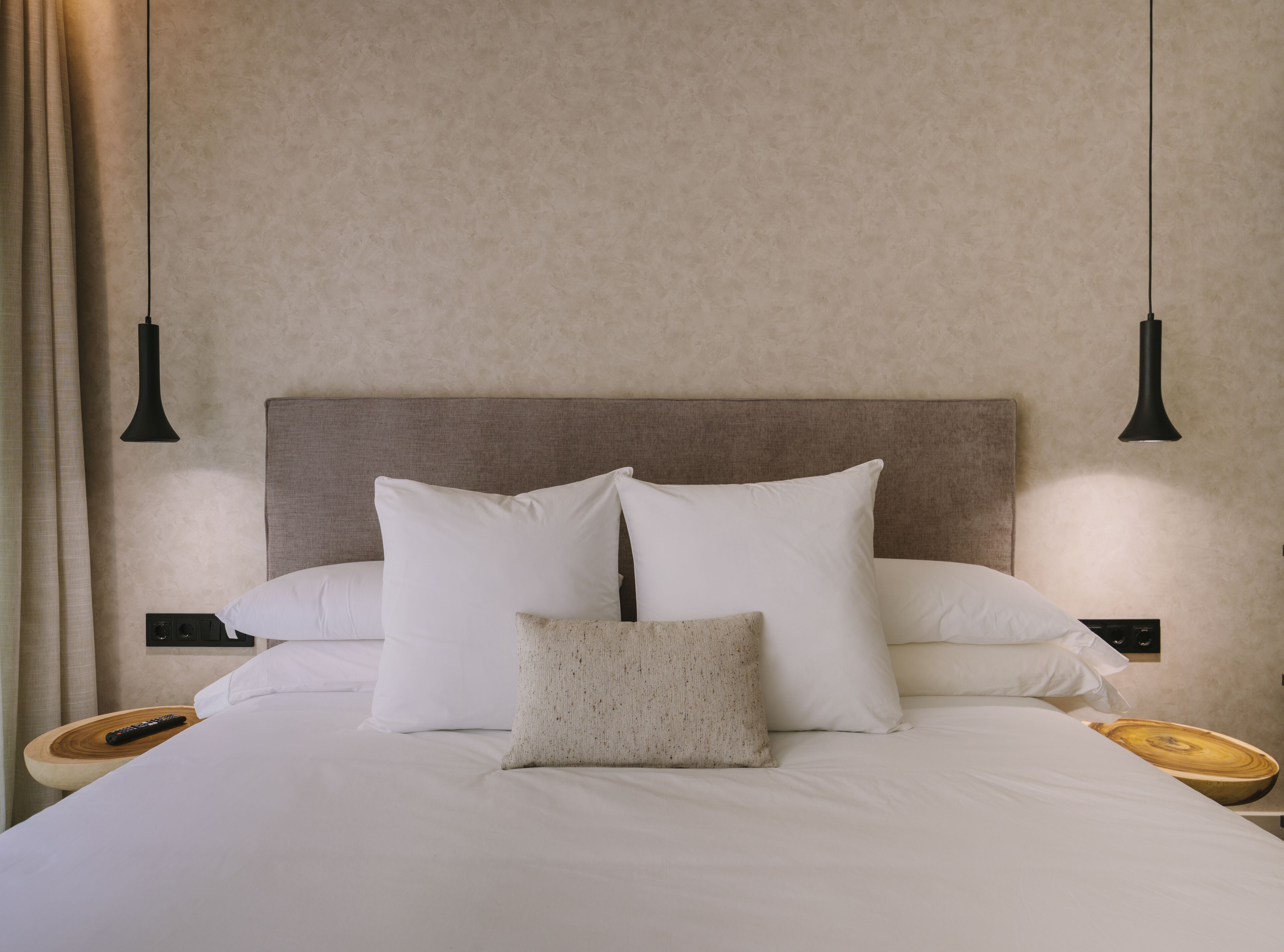 A neatly made bed with white linens and pillows, a wooden headboard, and two bedside tables with black lamps.