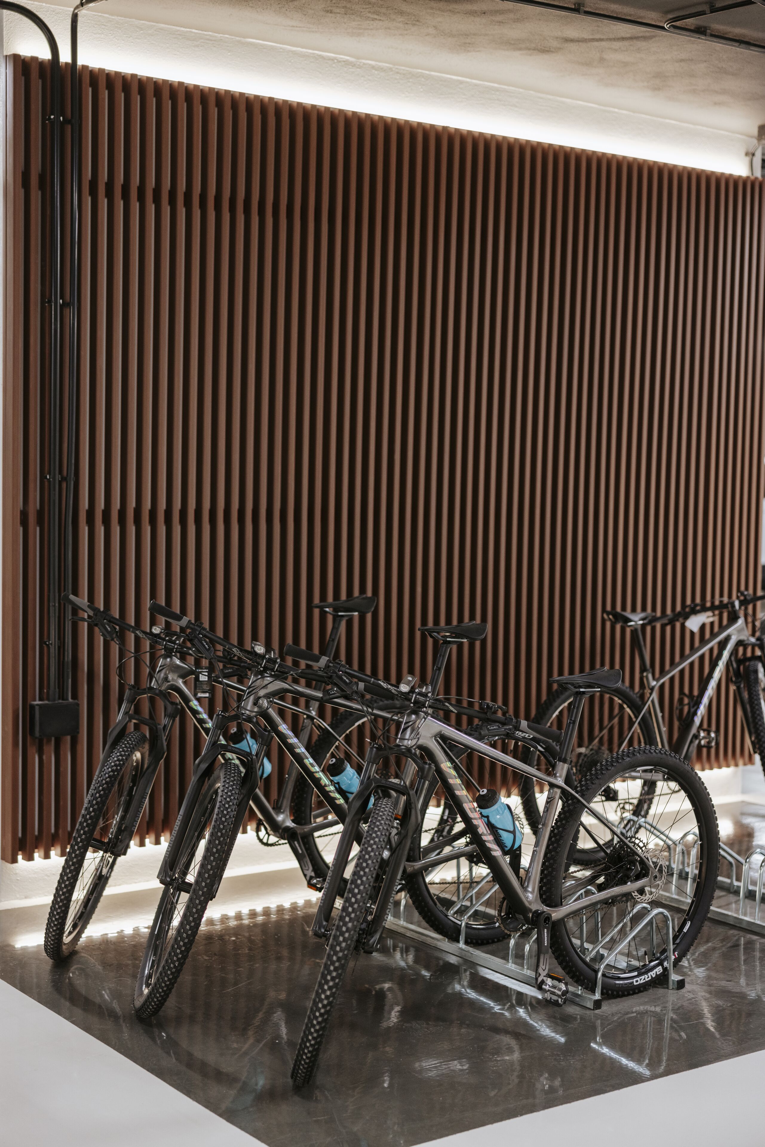 A bike rack with multiple bicycles parked against a wooden slat wall.