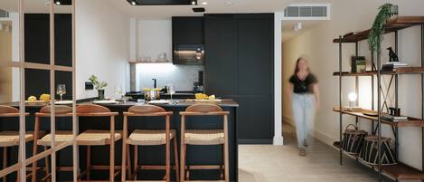Una cocina moderna con armarios oscuros, una isla central con taburetes altos y una persona caminando por el espacio.