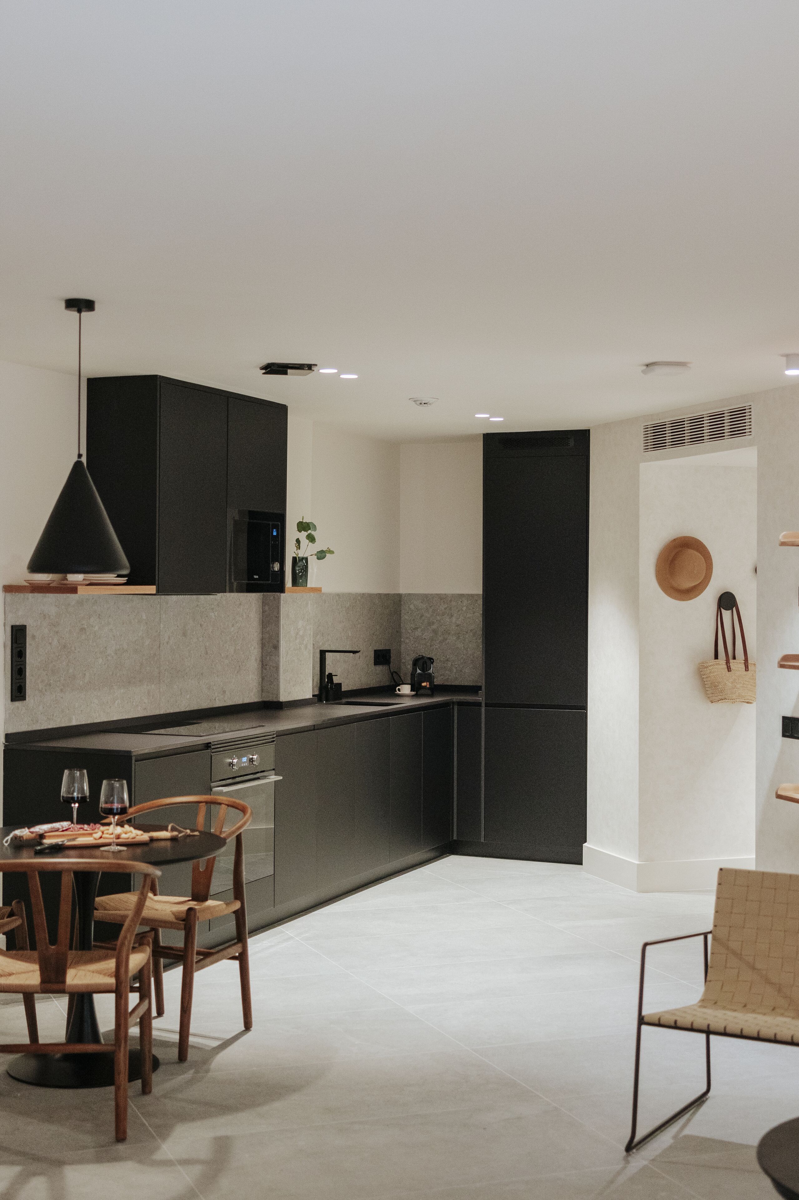 A modern kitchen with dark cabinetry, a central island, and a dining area with wooden chairs.