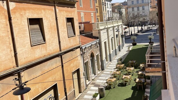 Un callejón estrecho con césped artificial verde, plantas en macetas y mesas al aire libre.