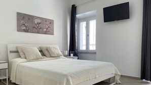 Un dormitorio con cama, mesita de noche, televisor de pantalla plana, ventana con cortinas y una obra de arte colgada en la pared.