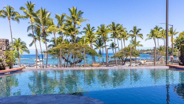 Une piscine à l’eau cristalline, entourée de palmiers et offrant une vue sur l’océan.