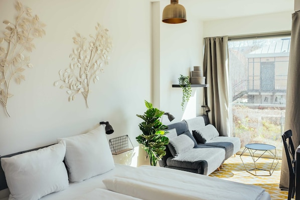 Ein modernes Schlafzimmer mit Schlafsofa, großem Fenster mit Vorhängen, einer Hängepflanze und einem kleinen Tisch.