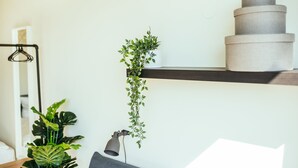 A room with a wooden desk, a hanging plant, a lamp, and a stack of storage containers on a shelf.
