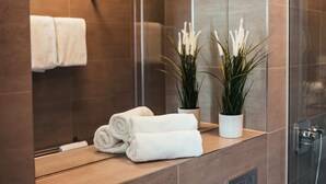 A bathroom with a mirror, two rolled white towels, and two potted plants.