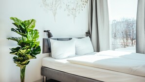 A modern bedroom with a large bed, a potted plant, and a wall art piece.