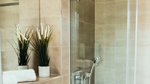 A modern bathroom with a glass-enclosed shower, a white sink, and two potted plants.