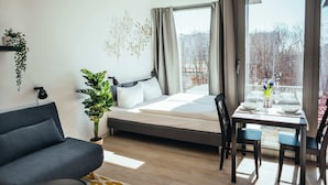 A modern bedroom with a bed, a sofa, a dining table with chairs, and a large window with curtains.