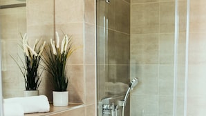 A modern bathroom with a glass-enclosed shower, a white sink, and two potted plants.