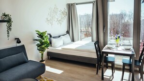 A modern bedroom with a bed, a sofa, a dining table with chairs, and a large window with curtains.