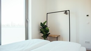 A bedroom with a bed, a potted plant, a floor lamp, and a window.