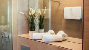 A modern bathroom with a glass shower enclosure, a mirror, and two potted plants.
