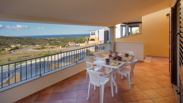A balcony with a table and chairs, a view of the sea, and a road in the distance. - Villa con Piscina - BUDONI (San Lorenzo)