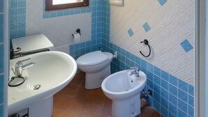 A bathroom with a sink, toilet, and bidet, tiled in blue and white, with a window above the toilet. - Villa con Piscina - BUDONI (San Lorenzo)