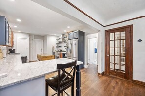 Una cocina moderna con encimera de mármol, piso de madera y una gran puerta de madera con paneles de vidrio.