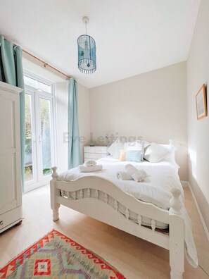 A bedroom with a white bed, a patterned rug, and a view of greenery outside.