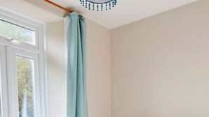Ein Schlafzimmer mit einem Bett, einem Nachttisch, einer Lampe und Blick durch ein Fenster mit Vorhang.