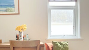 Ein Essbereich mit einem Holztisch und Stühlen, einer Vase mit gelben Blumen und einem Fenster mit Jalousien.