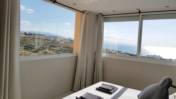 A hotel room with a large window offering a view of a coastal landscape. - House (Bahía de Casares)