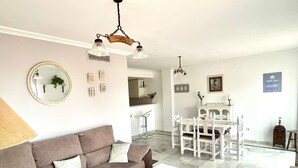 A living room with a sofa, coffee table, and dining area with chairs. There is a mirror on the wall and a hanging light fixture. - House (Bahía de Casares)