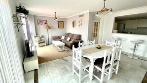 A spacious living room with a white sofa, a dining table with white chairs, and a kitchen area in the background. - House (Bahía de Casares)