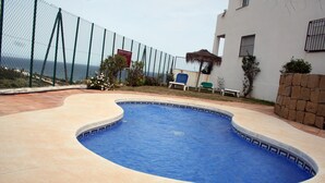 A swimming pool with a curved edge, surrounded by a tiled deck. There is a fence enclosing the area, and a bench is visible near the fence. - House (Bahía de Casares)