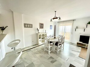 A dining area with a white table and chairs, a white cabinet, and a television on a stand. - House (Bahía de Casares)
