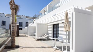 A modern outdoor lounge area with white furniture, a palm tree, and a clear blue sky. - Esmeralda Cotillo Homes by LIVVO (La Oliva)